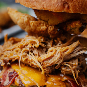 A close-up of a stacked pulled pork sandwich with melted cheese, bacon, and fried onions_jalapeños on a bun