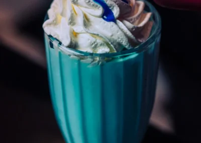 A hand squeezing blue syrup onto whipped cream topping a bright blue or teal milkshake