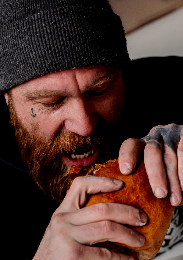 A person wearing a beanie and a black hoodie eating a burger