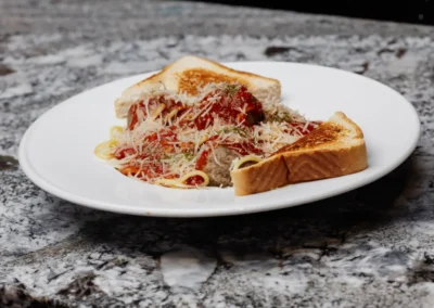 A plate of spaghetti and meatballs topped with sauce and Parmesan cheese, served with two slices of buttered toast