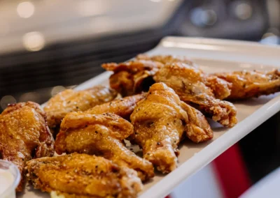 A platter of glazed, baked chicken wings served with celery sticks and a dipping sauce on a white tray