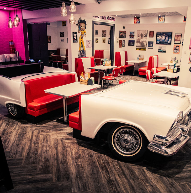 A retro diner featuring a white and red car-shaped booth with classic decor and bright seating, evoking a nostalgic atmosphere
